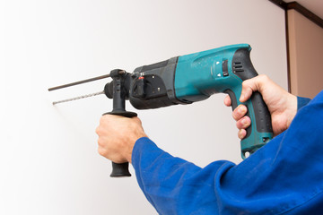 Construction worker is boring the wall by electric perforator