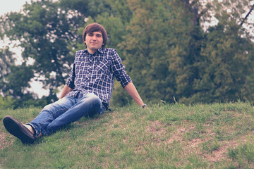 Naklejka na ściany i meble Portrait of young smiling handsome man sitting on the green grass