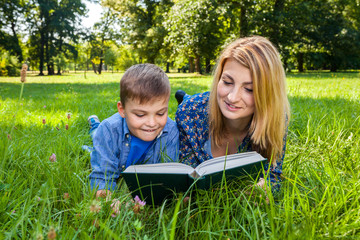 young mother and son lying on the meadow with book