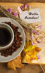 The cup of coffee lying ot the opened book with maple leaves