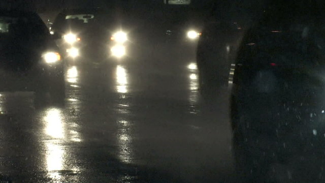 The headlights of rush hour traffic coming home in a blizzard reflect off the pavement
