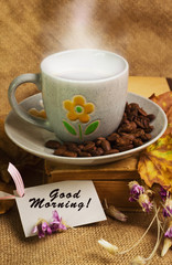 The cup of coffee lying ot the book with maple leaves