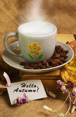 The cup of coffee lying ot the book with maple leaves