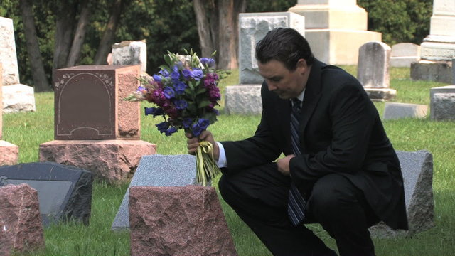 Man with flower bouquet visits a grave at a cemetery
