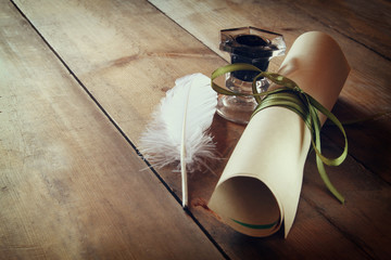 photo of white Feather and scroll paper on old wooden table.
