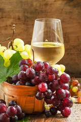 White wine in a glass and green and red grapes in a wicker baske