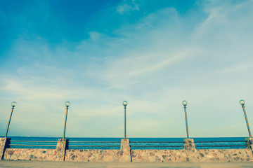 Obraz premium Lamp post and stone fence on road beside blue sea in vintage sty