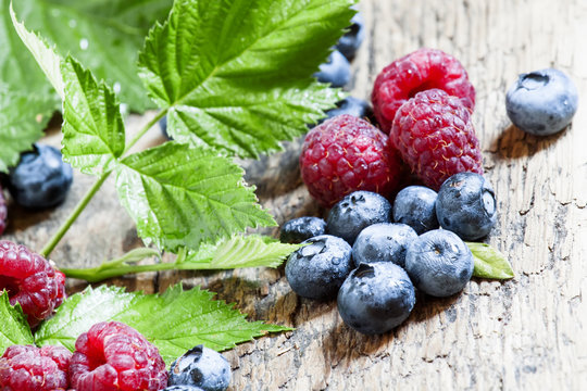 raspberries and blueberries with leaves on the old wooden backgr