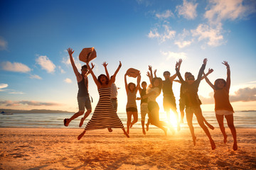 happy young people jumping at the beach on beautiful sunset