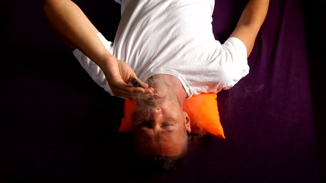 man lying on bed and vapouring e cigarette. vapor is visible, footage taken with wide angle lens and dslr camera, sunlight comes from window.
