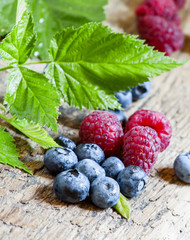 raspberries and blueberries with leaves on the old wooden backgr