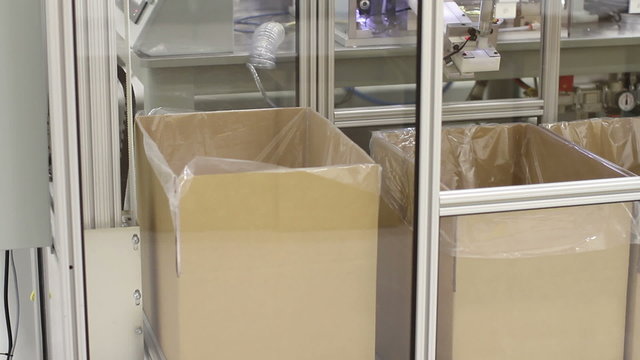 An entirely automated manufacturing process in a factory, with a box being filled with product, then moved out of the way through the conveyor system, making room for the next box.
