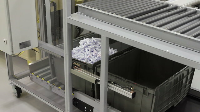 Camera follows the movement of a plastic bin in a factory, as it fills up with small plastic parts, then moves through an automated conveyor system and moved aside.  
