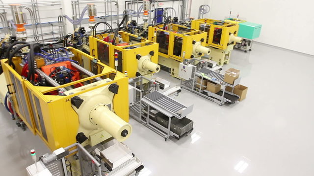 Panning across a factory floor from a high angle, showing multiple large injection molding machines. 
