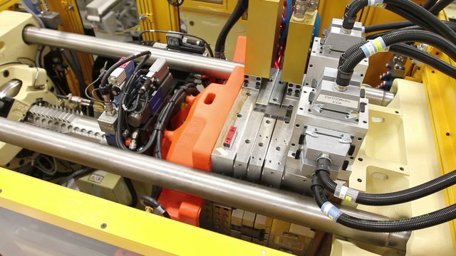 A wider shot cuts to a close-up of an injection molding machine in a factor
