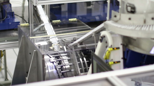 A close-up and a wide angle shot of small plastic parts (chapstick) being assembled by a large industrial machine in a factory
