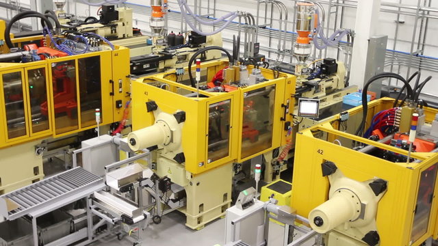 Tracking along a factory floor from a high angle, showing multiple large injection molding machines. 
