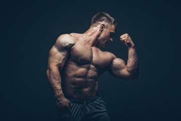 Fototapeta na wymiar Handsome muscular bodybuilder posing over black background.