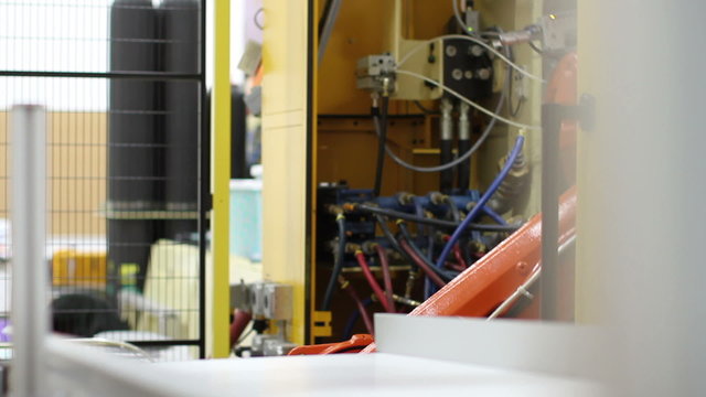 A robotic arm in a factory, as it grabs a plastic product from an injection molding machine and carries it to another machine to apply a label. 
