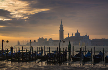 Fototapeta premium Gondolas by Saint Mark square during sunrise with San Giorgio di Maggiore church in the background in Venice Italy
