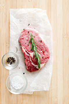 Raw steak on wooden surface with salt and pepper