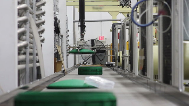 looking down a conveyor belt in a factory as robotic arms deliver plastic products onto the conveyor belt
