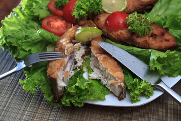 A piece of fried fish fillett served on blue glass table with lettuce, lime, tomato and herbs