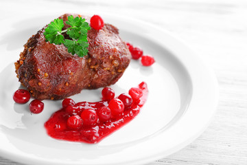 Tasty roasted meat with cranberry sauce on plate, on color wooden background