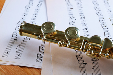 Obraz premium Silver flute with music notes on wooden table close up
