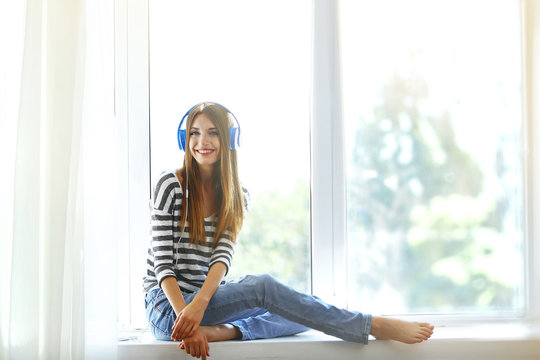 Woman listening music in headphones on windowsill background