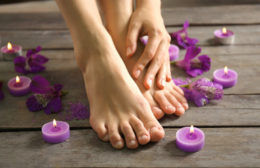 Female feet at spa pedicure procedure with flowers and candlelight on wooden background