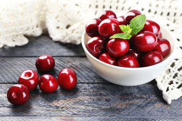Sweet cherries with green leaves in bowl, on wooden background