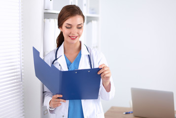 Smiling female doctor with a folder in uniform standing at