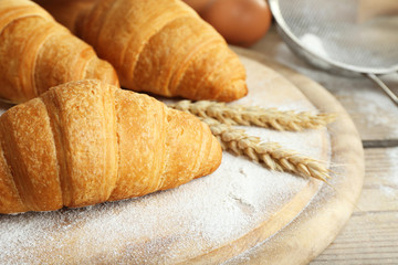 Fresh croissants with flour on wooden table, closeup