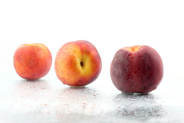 three ripe peaches in the water droplets on white background