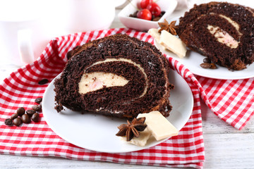 Delicious chocolate roll in white saucer on checkered napkin, closeup