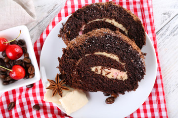 Delicious chocolate roll in white saucer on checkered napkin, closeup
