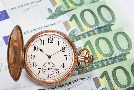 Time is money concept with hundred euros bills and golden pocket watch.