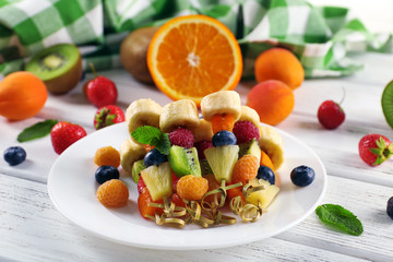 Fresh fruits on skewers in plate on wooden table, closeup