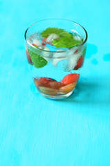 Glass of cold refreshing summer drink with berries and ice cubes on table close up