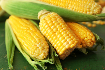 Fresh corn on cobs on green wooden table, closeup
