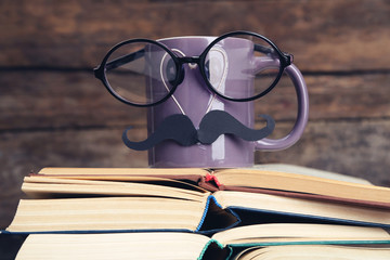 Vintage books and cup with mustache on wooden background