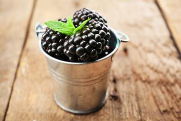 Fototapeta na wymiar Ripe blackberries with green leaves in small metal bucket on wooden background