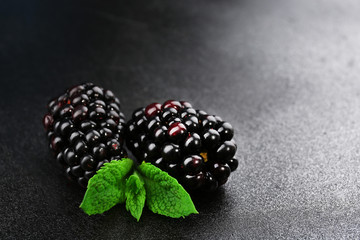 Ripe blackberries with green leaves on dark surface, closeup