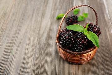Fototapeta na wymiar Ripe blackberries with green leaves in wicker basket on wooden background