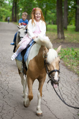 Little girl riding on a pony in a city park