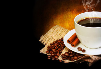 Coffee cup with saucer and coffee beans on burlap over dark 