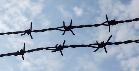 Two barbed wire silhouette with blue sky and clouds background.