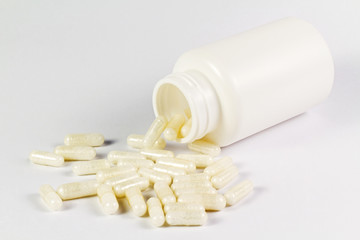 Capsules spilling out of a bottle on the white background.