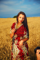  woman with ornamental dress standing on wheat field sunset.